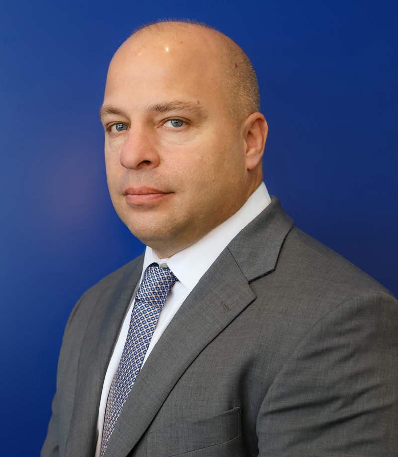 Jerret Giammichele, Vice President of Sales and Marketing, wearing a gray suit, standing in front of a blue background